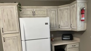 Una cocina con muebles blancos, un refrigerador blanco, un tostador y un cubo de basura.