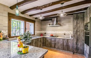 Une cuisine avec des meubles en bois, un plan de travail en granit, une fenêtre à barreaux et des luminaires suspendus.