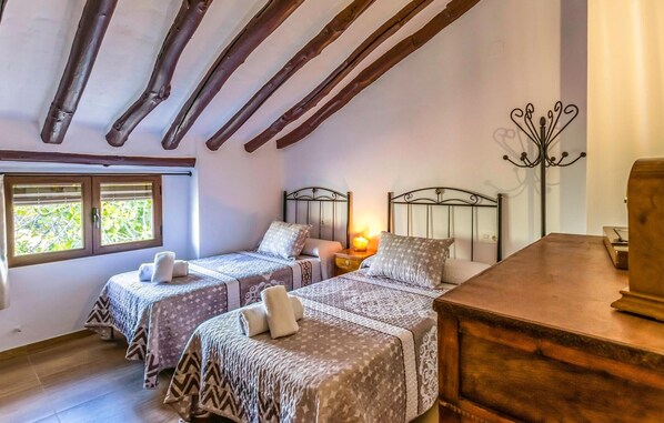 A cozy bedroom with two beds, wooden beams, a nightstand with a lamp, and a dresser. - Cozy home in Puertollano (Puertollano)