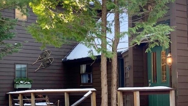 A wooden cabin with a deck, surrounded by trees and covered in snow. - Woody Creek On-Mountain Ski House - 6 Bedroom, Sleeps 10, Pool Table (Carrabassett Valley)