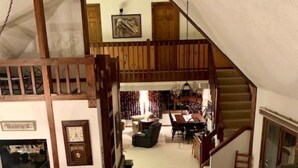 A spacious loft with a high ceiling, exposed wooden beams, a fireplace, and a cozy seating area. - Woody Creek On-Mountain Ski House - 6 Bedroom, Sleeps 10, Pool Table (Carrabassett Valley)