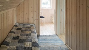 Een kamer met houten wanden en een schuin plafond, een kleurrijke quilt op het bed, een kleine tafel en een stoel.