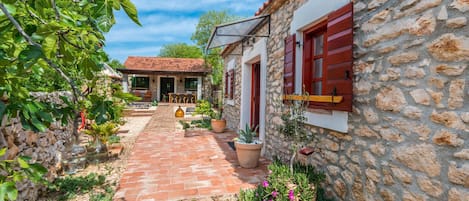 A stone building with red shutters, a brick pathway, and potted plants.