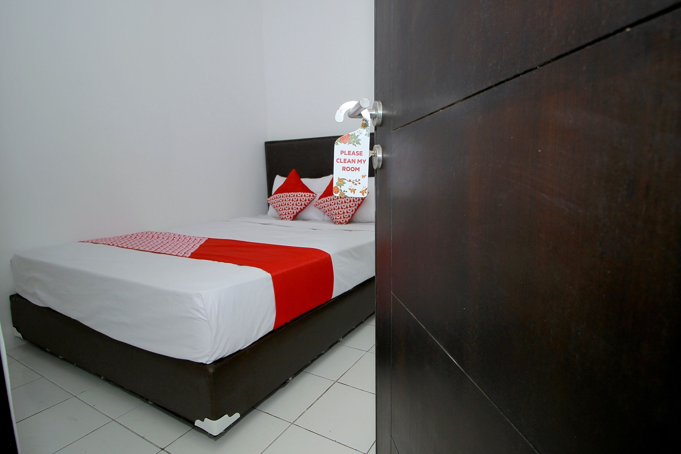 Una cama individual con una colcha blanca y roja, dos almohadas rojas y un cabecero de madera.