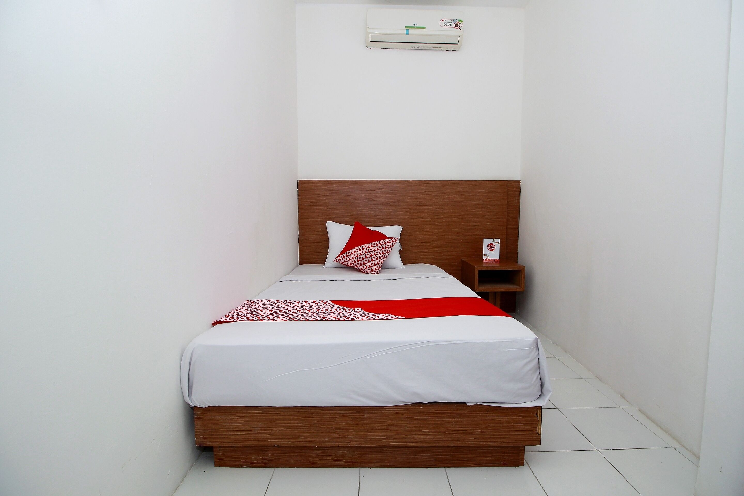 A single bed with a wooden headboard, white bedding, and a red and white patterned throw.