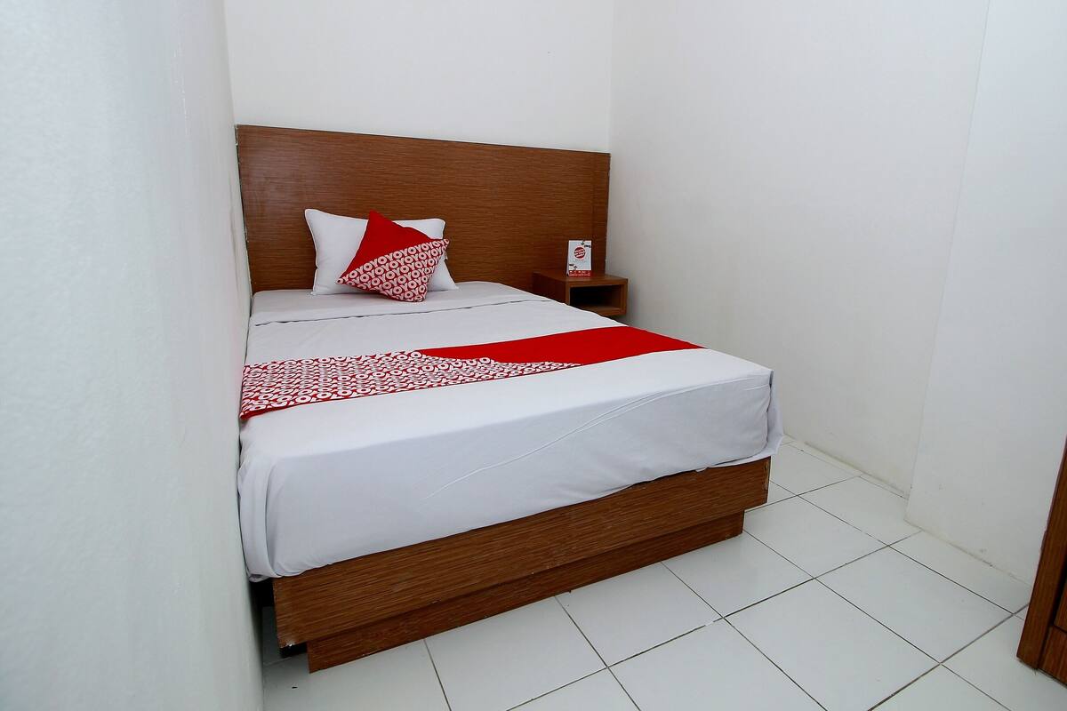 Een net opgemaakt bed met een houten hoofdbord, witte beddengoed en een rode en witte gestreepte deken.