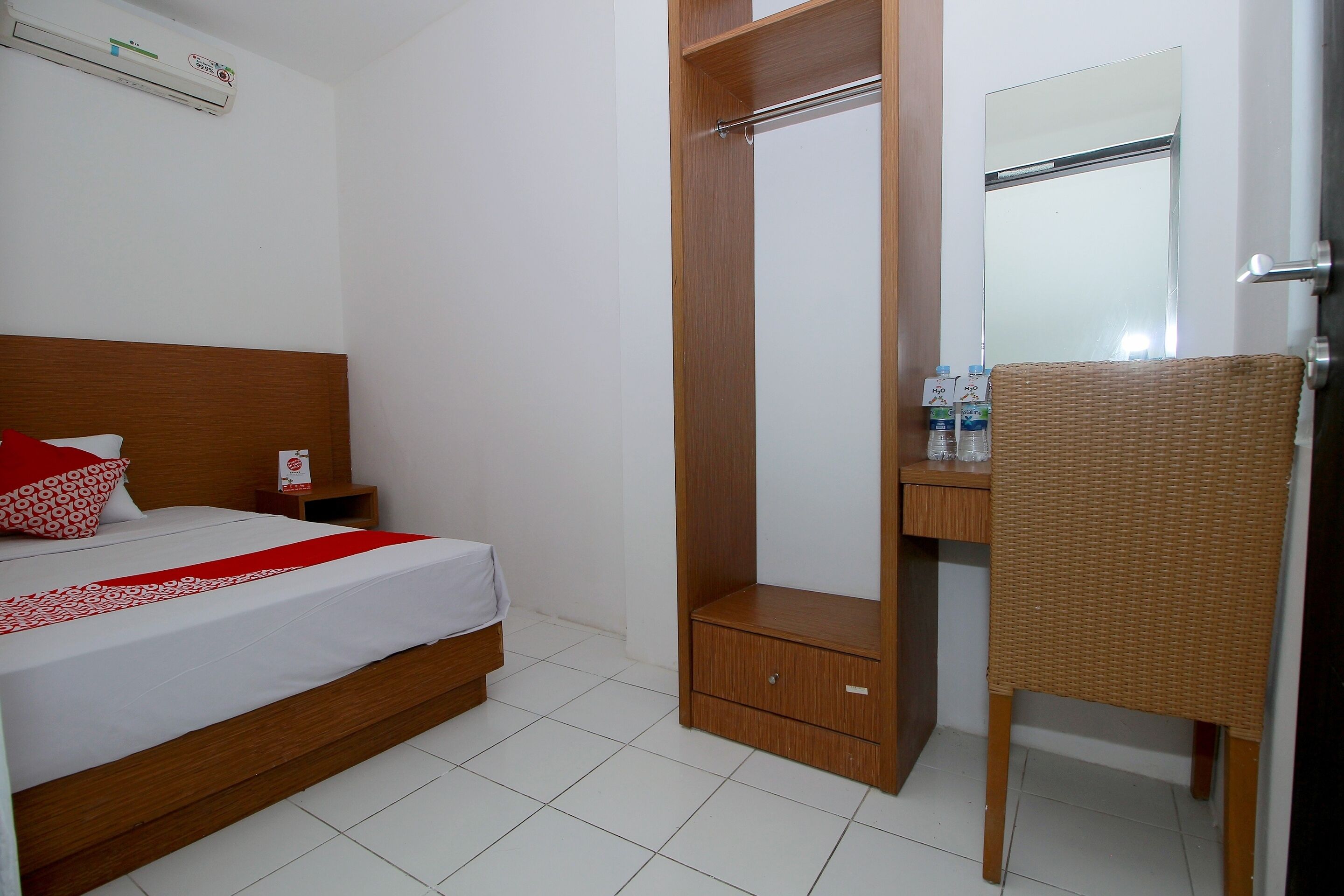 A hotel room with a bed, a wooden wardrobe, a mirror, and a wicker chair.