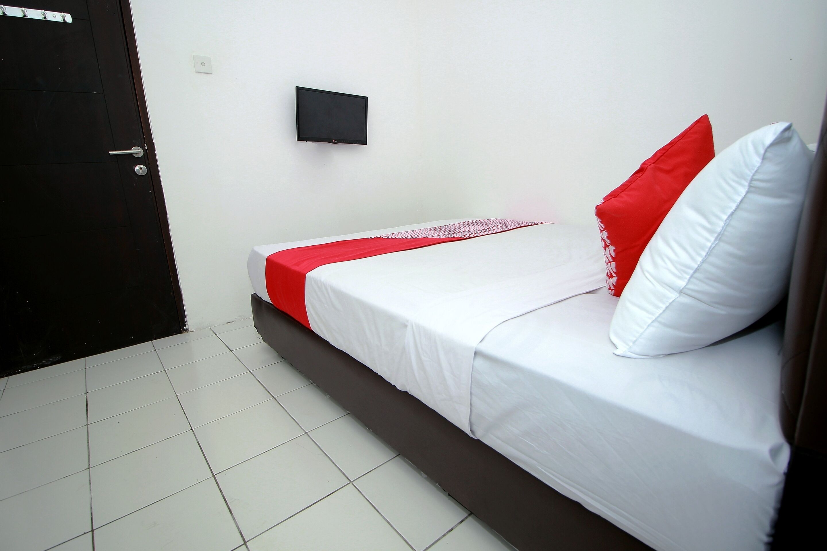 A hotel room with a bed, a flat-screen TV mounted on the wall, and a door.