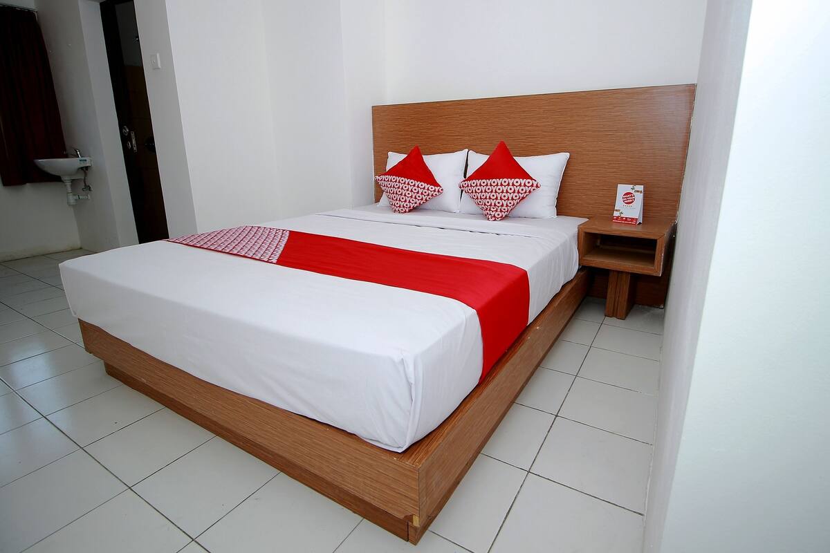 Een hotelkamer met een houten bed, witte beddengoed en een rode accentkleur.