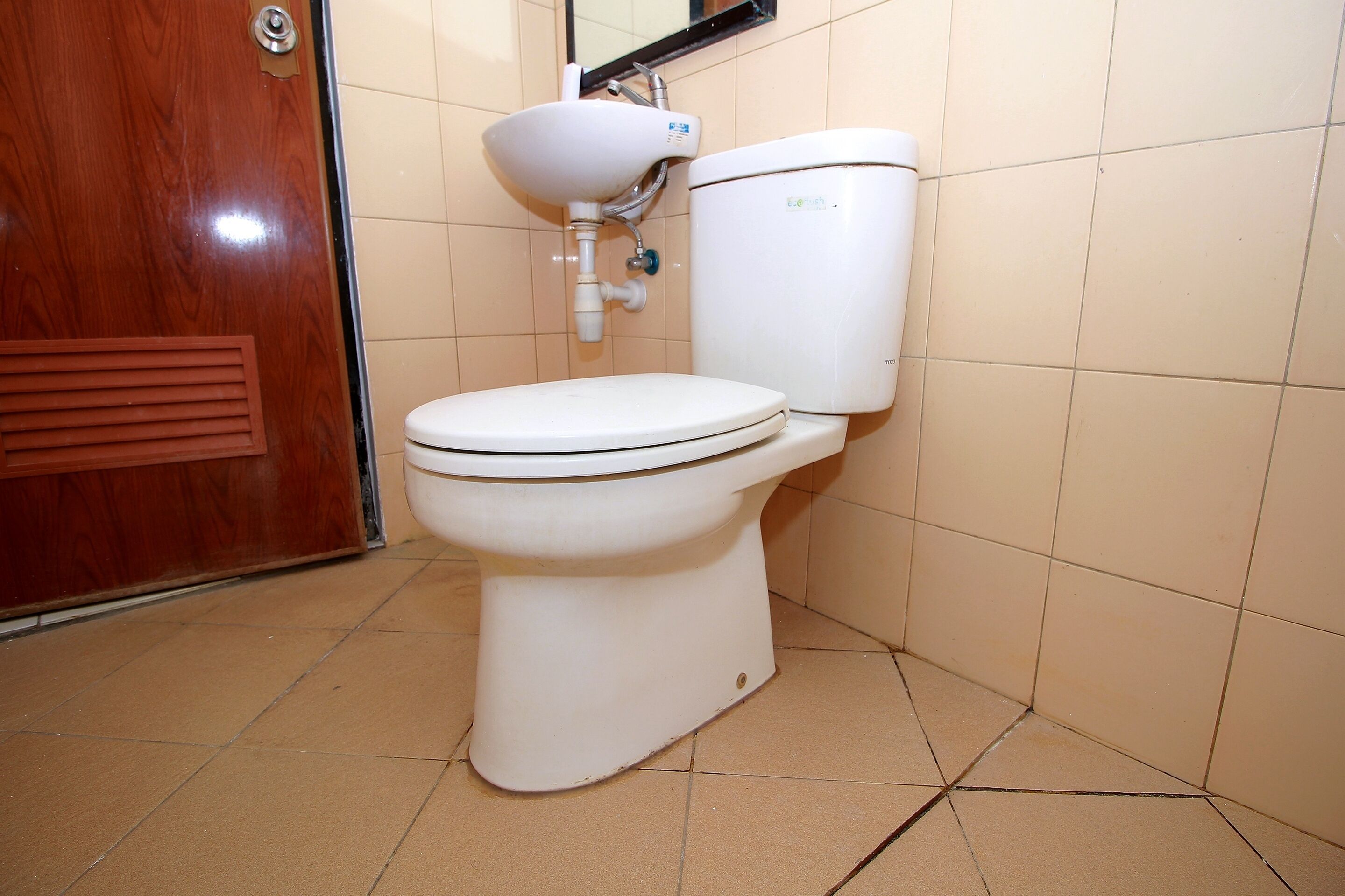 A white toilet with a tank and a bidet attachment in a bathroom with beige tiles.