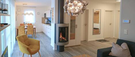 Een moderne woonkamer met een bank, een gele fauteuil, een bijzettafeltje met een boek en kaarsen, en een open haard.