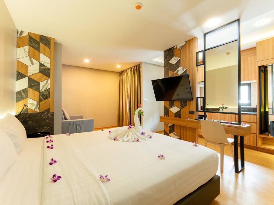 A hotel room with a large bed, a desk, a chair, a TV, and a mirror.