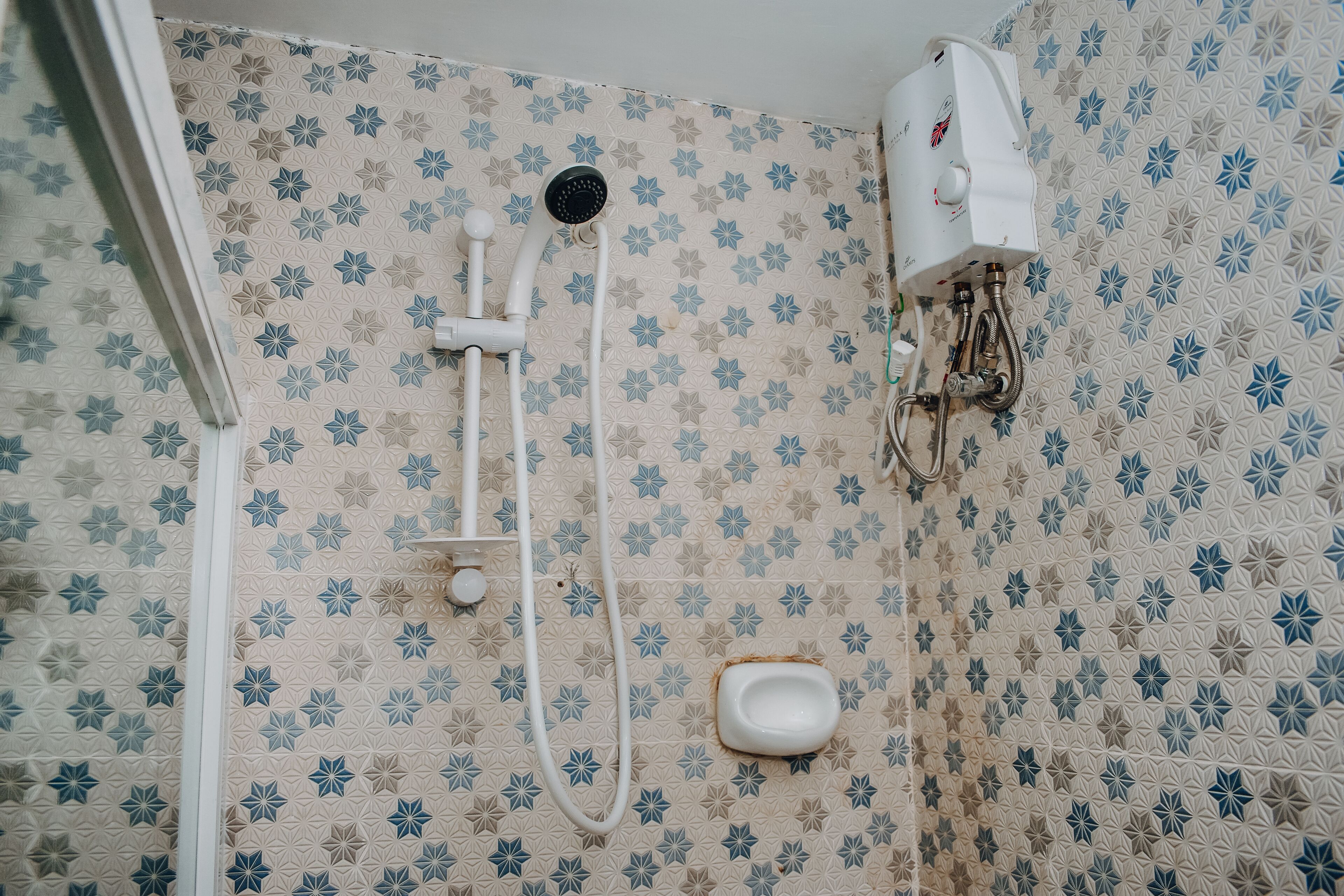 A shower area with a handheld showerhead, a wall-mounted water heater, and a toilet.