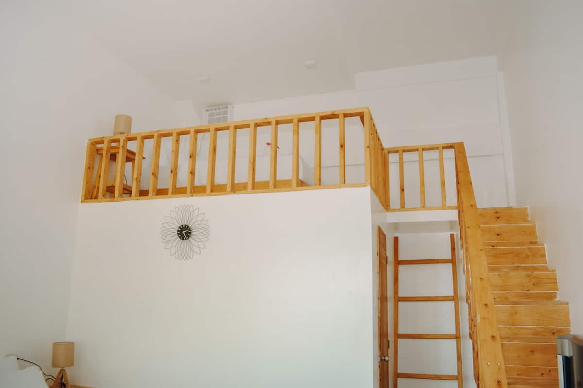 Una escalera de madera con barandilla que lleva a un altillo.