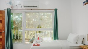 Habitación de hotel con cama, mesita de madera, ventana con cortinas y equipo de aire acondicionado.
