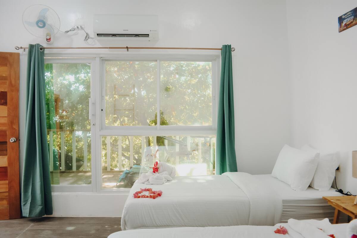 Habitación de hotel con cama, mesita de madera, ventana con cortinas y equipo de aire acondicionado.