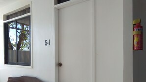 Una habitación con un banco de madera, una puerta blanca y un ventanal con vistas a palmeras.