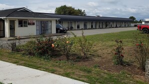 Un motel con una fila de habitaciones, zona de estacionamiento y un césped con flores.