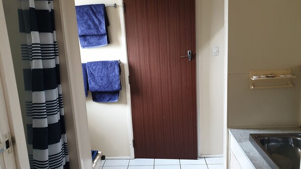 Un baño con puerta de madera, suelo de baldosas blancas y un toallero con toallas azules.