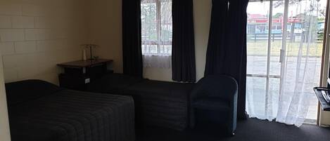 A small, dimly lit room with two single beds, a desk, and a chair.