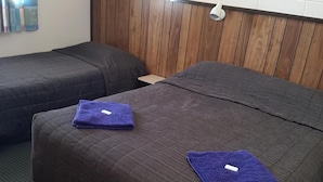 Habitación de hotel con dos camas, cada una con una toalla morada y un cabecero de madera.