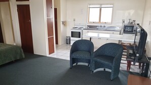 Una habitación pequeña con kitchenette, dos sillas, una mesa y una cama con cubierta verde.