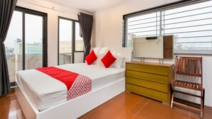 A modern hotel room with a large bed, a wooden dresser, and a window with blinds.