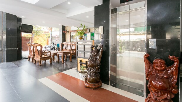 A lobby with a reception desk, wooden chairs, a statue, and an elevator.