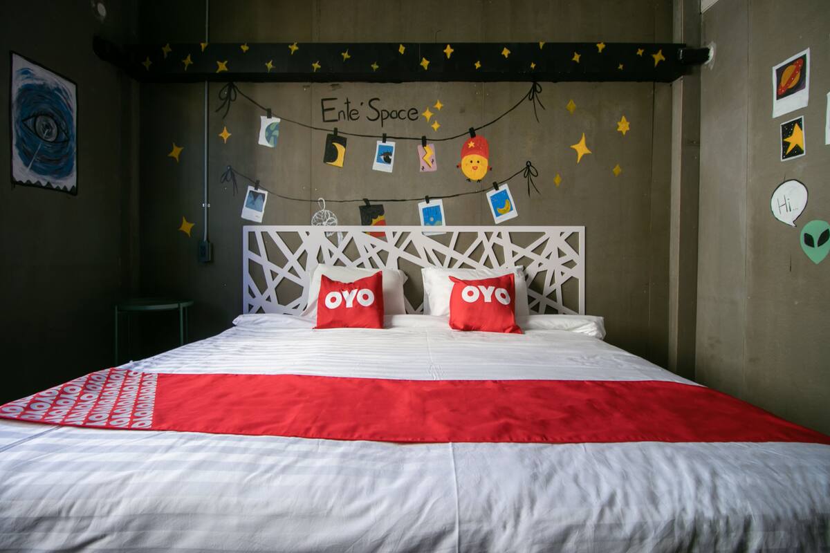 A bedroom with a bed, white and red bedding, a white headboard, and a wall decorated with star patterns and a string of pictures.