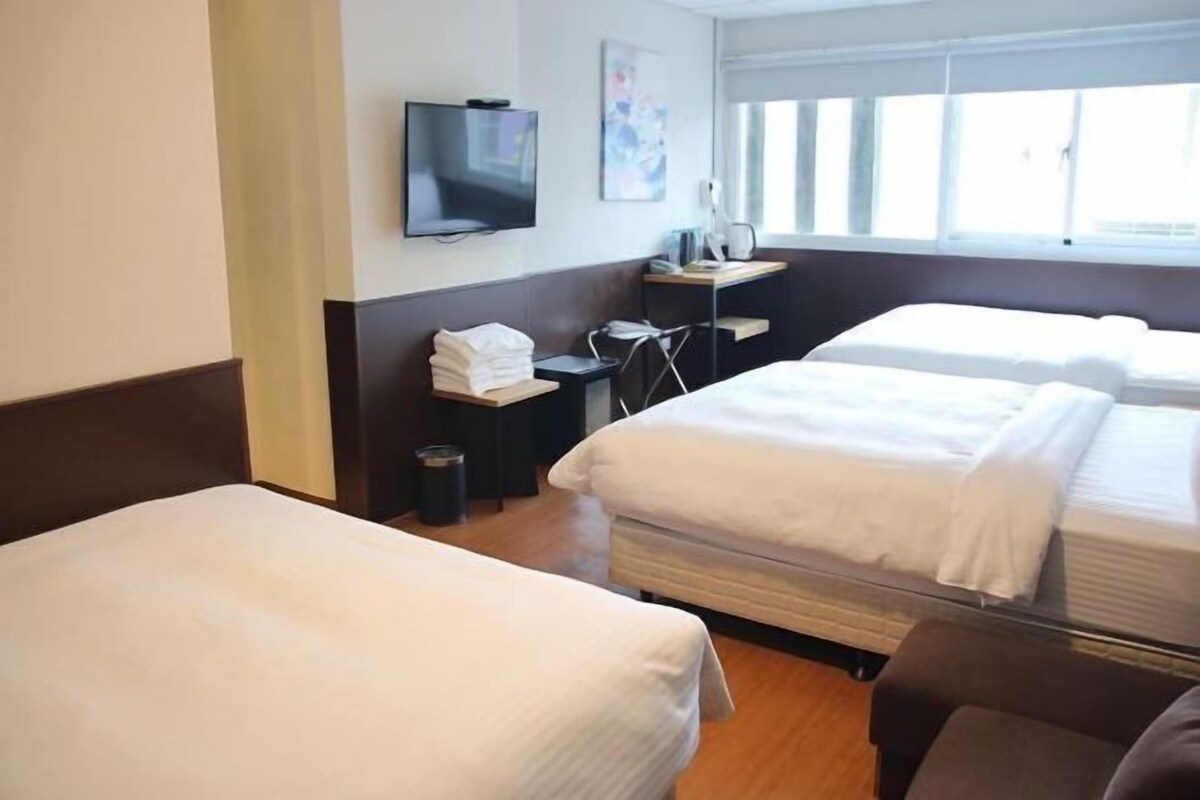 Habitación de hotel con dos camas, televisor, escritorio y silla, y una ventana.