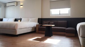 A modern hotel room with a bed, a sofa, a small table, and a window. - Cloud Haku Cozy Inn (Taitung)