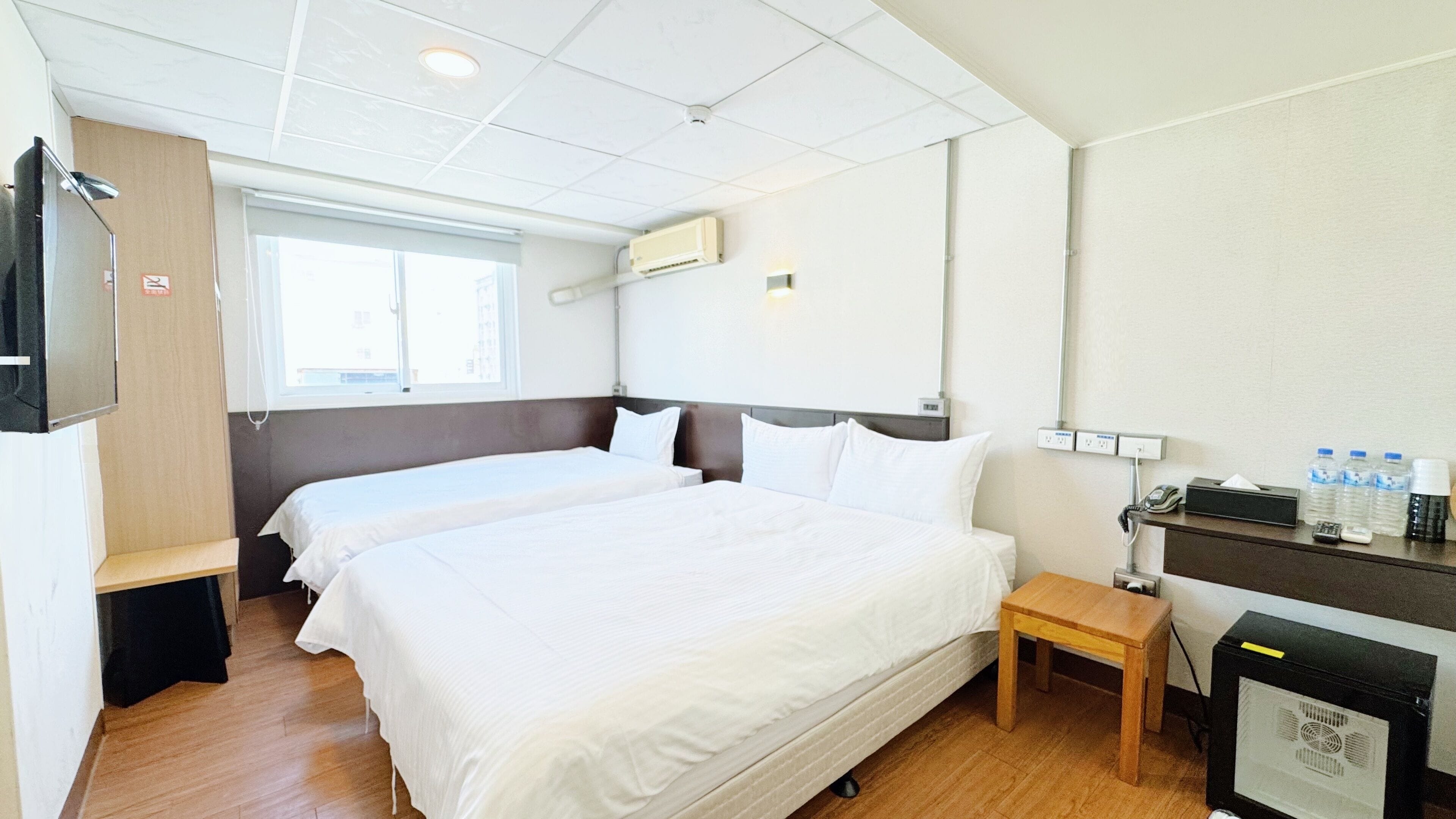 Hotellihuone, jossa on kaksi sänkyä, työpöytä, tuoli, televisio ja minibaari.