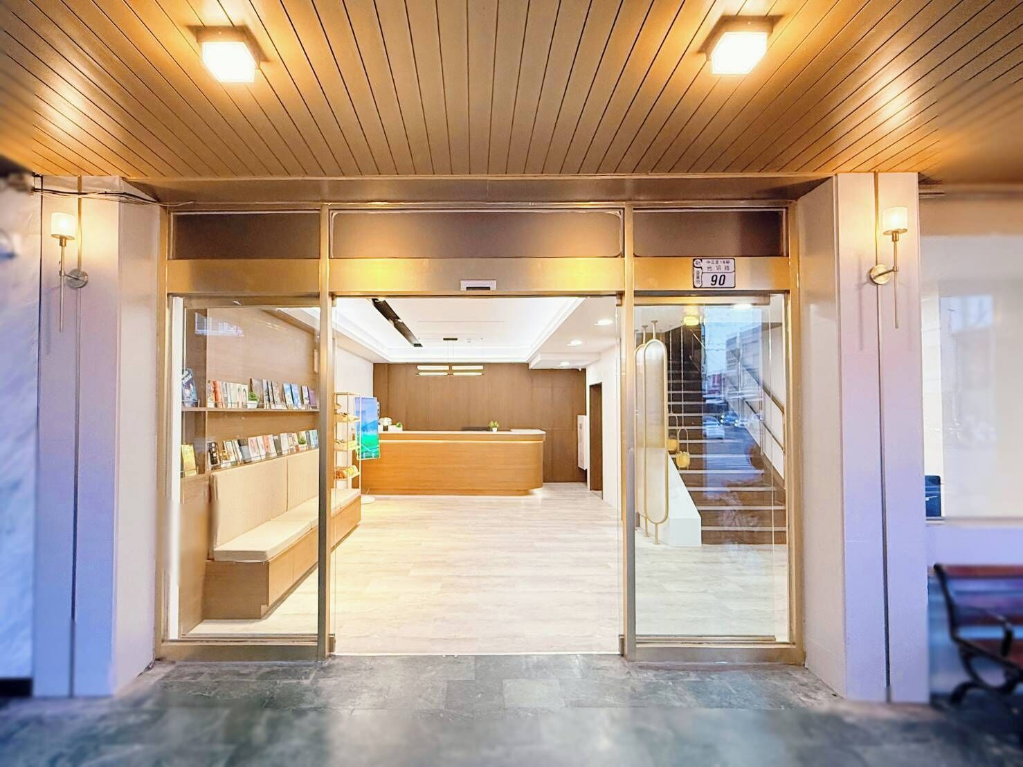 A hotel reception area with a reception desk, a staircase, and a glass door entrance.