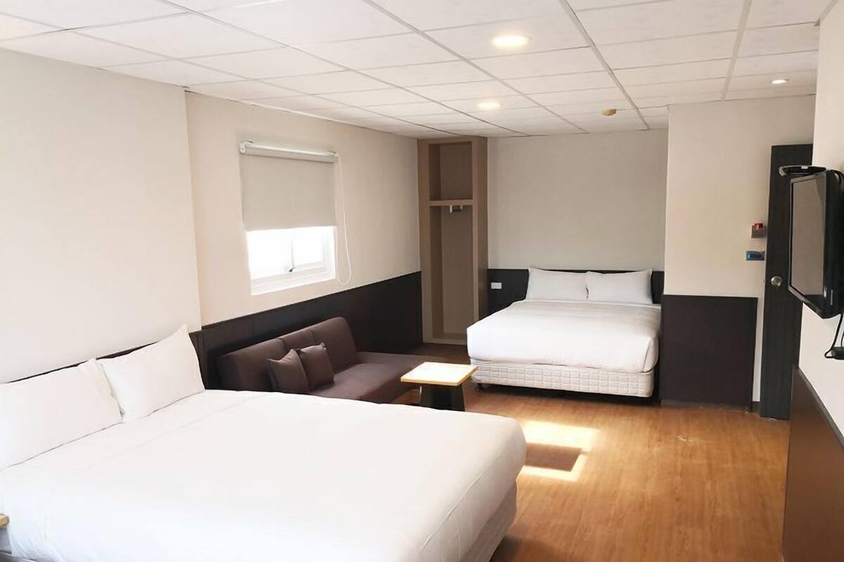 Habitación de hotel con dos camas, un sofá, una mesita y un televisor.