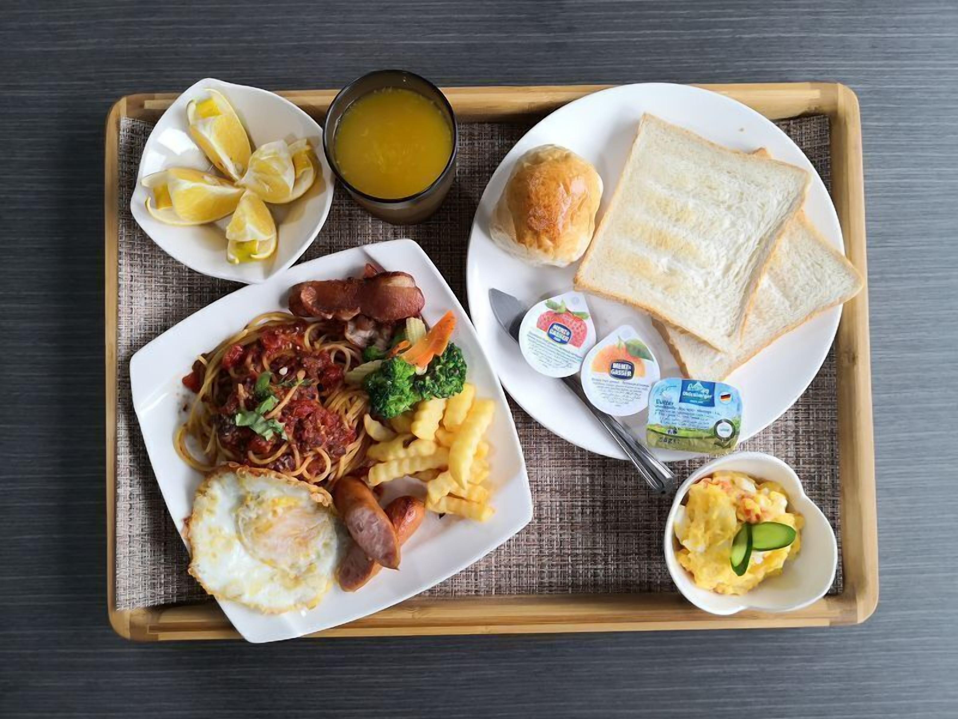 A tray with breakfast items including eggs, sausage, pasta, toast, and fruit.