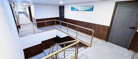 A hotel interior with a staircase, a wooden wall panel, a door, and a painting on the wall.