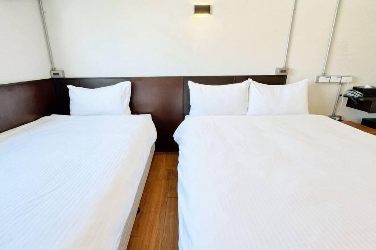 Habitación de hotel con dos camas, suelo de madera y una lámpara fijada a la pared.