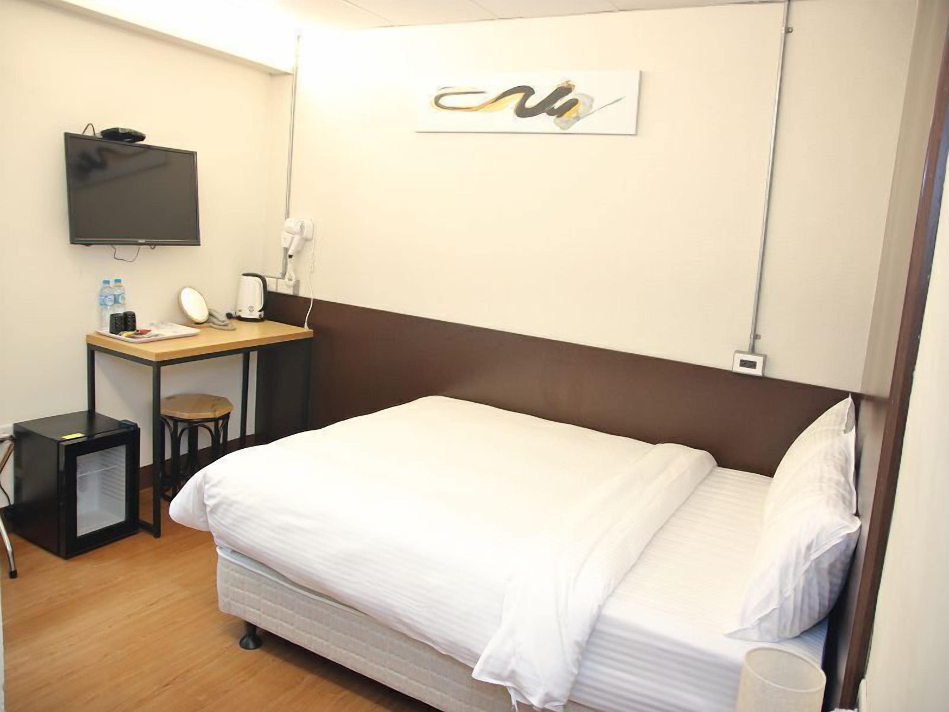 Habitación de hotel con una cama, un escritorio con una silla, un televisor y una obra de arte en la pared.