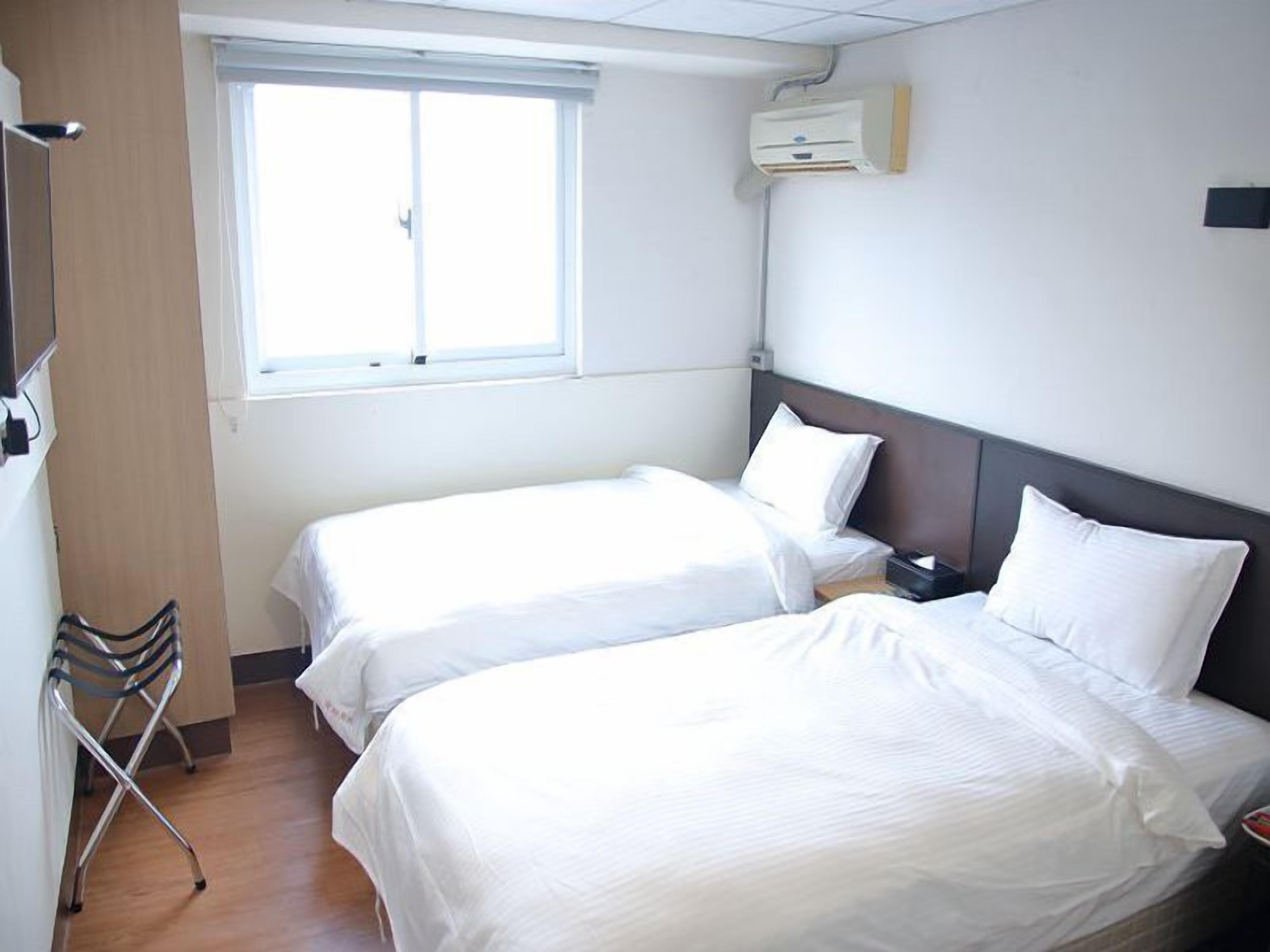 Habitación de hotel con dos camas, una ventana, un equipo de aire acondicionado y una silla.