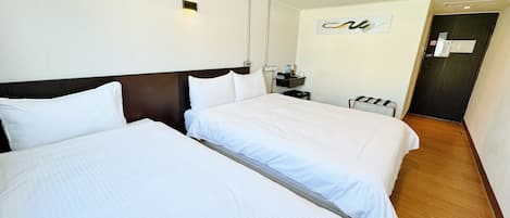 A hotel room with two beds, a nightstand, a wall-mounted light, and a door.