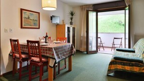 Ein Essbereich mit einem Tisch für vier Personen, einer Couch, einem Fernseher und einer Schiebetür zu einem Balkon.