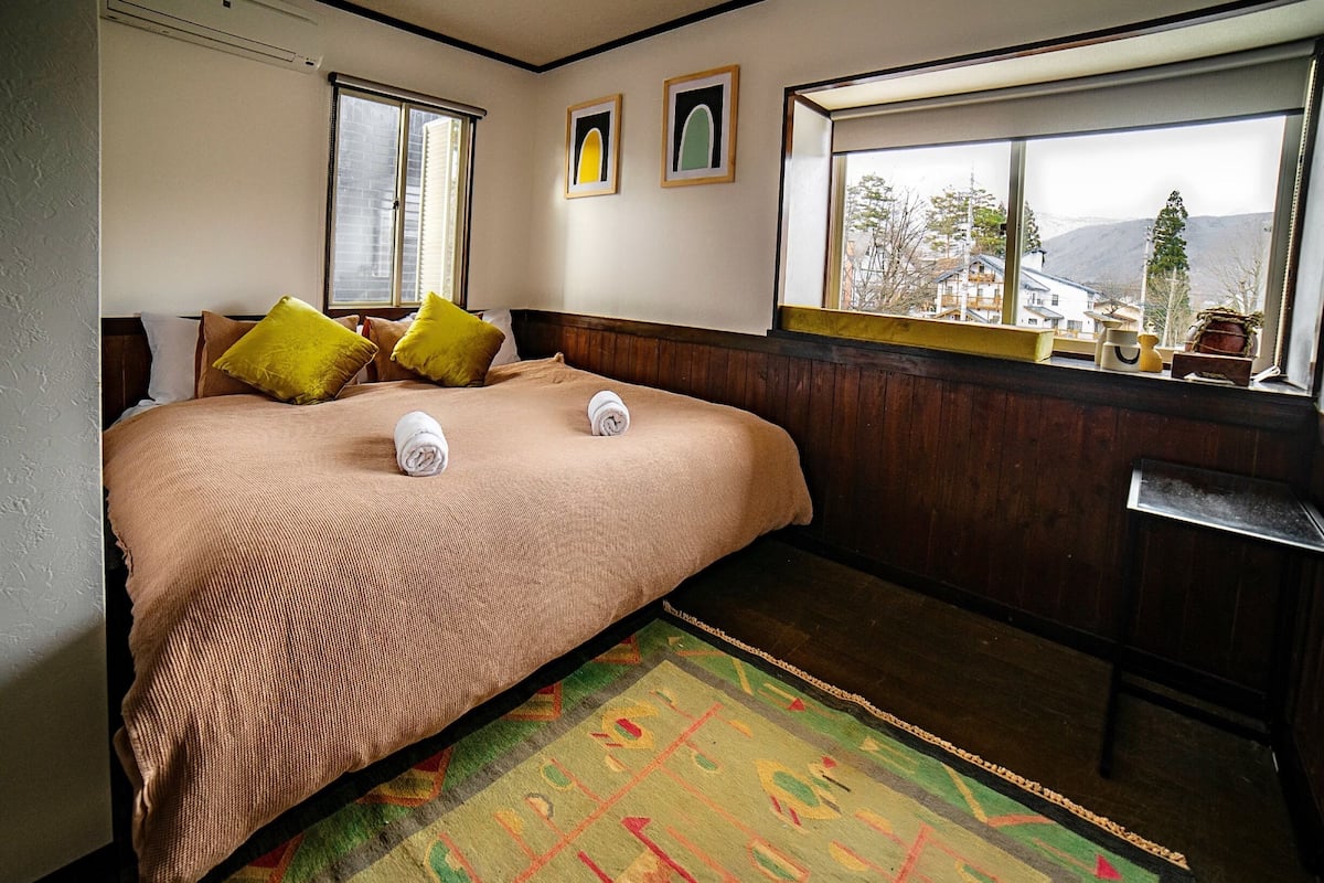 Une chambre dâhĂŽtel avec un grand lit, deux oreillers, une fenĂȘtre donnant sur un beau paysage et une commode en bois.