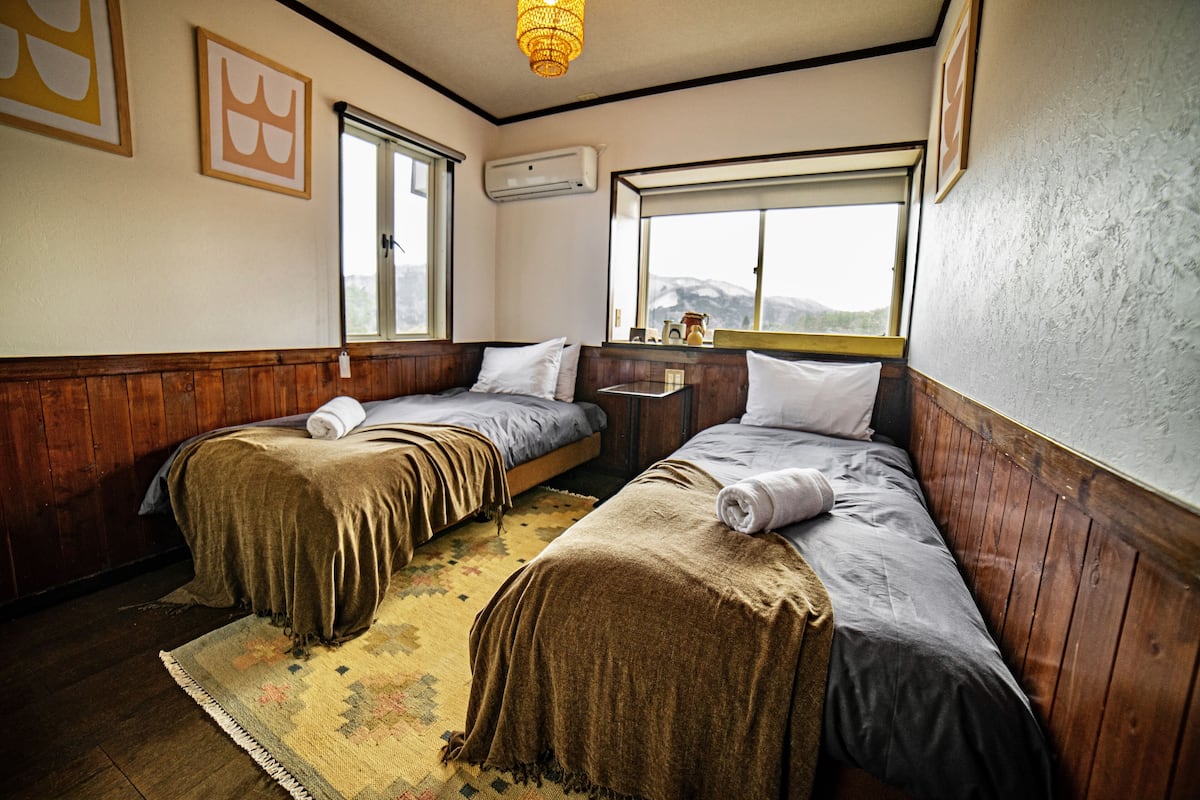 Une chambre avec deux lits, des murs en bois, une fenĂȘtre donnant sur la montagne et un appareil de climatisation.