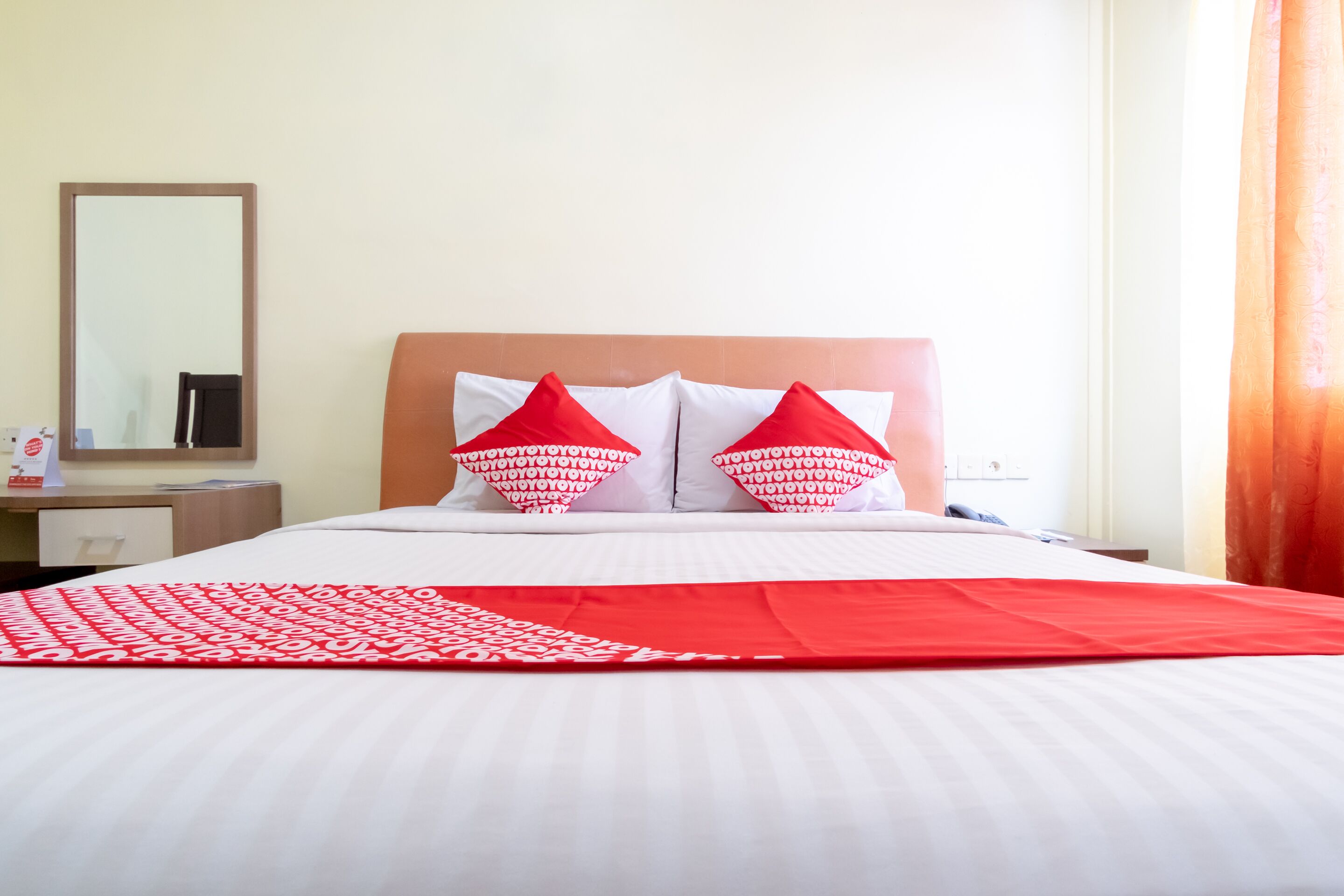 A hotel room with a bed, two red pillows, a white bedspread, and a red blanket.