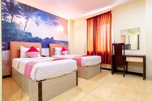 A hotel room with two beds, a desk, and a large painting of a tropical landscape.