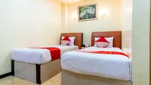 Dos camas individuales con ropa de cama roja y blanca, un cuadro en la pared y una mesita con una botella.
