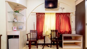 Un espacio habitable compacto con una pequeña cocina americana, una zona de comedor con dos sillas y una mesa, un televisor montado en la pared y una ventana con cortinas rojas.