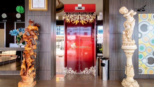 Entrada de hotel con un ascensor rojo, una escultura de madera y una estatua sobre un pedestal.