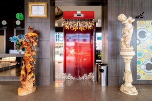 A hotel entrance with a red elevator, a wooden sculpture, and a pedestal statue.