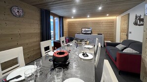 Een gezellige kamer met houten wanden en plafond, een eettafel gedekt met borden, glazen en bestek, een bank en een televisie op een kast.